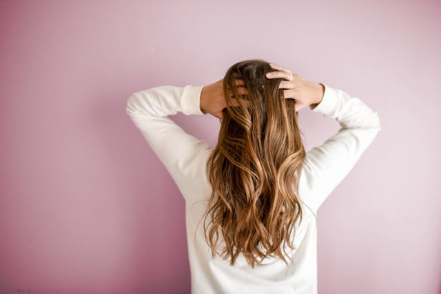 woman scratching the back of her head in front of a pink wall